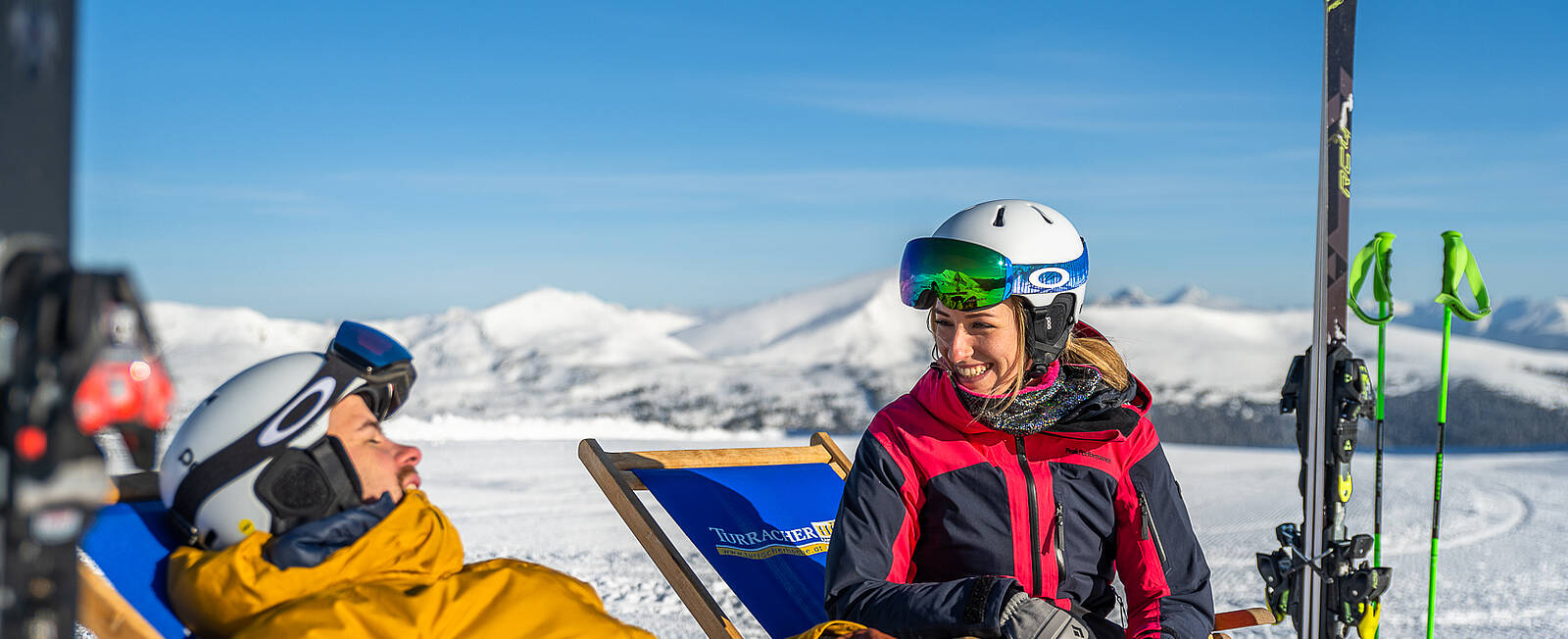 2 Personen sitzen in Liegestühlen, genießen die Sonne und haben Spaß miteinander