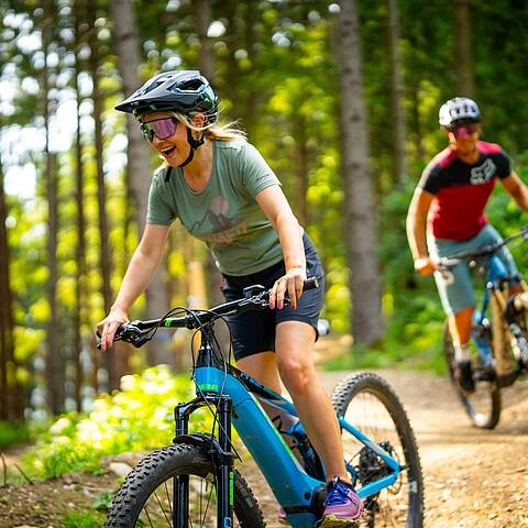Zwei Mountainbiker fahren hintereinander mit ihren Bikes einen Trail im Skillscenter der Bike Area Obermillstatt hinunter