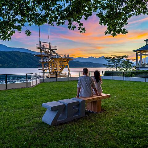 Pärchen sitzt am Abend auf Zeitbank und sieht sich den Sonnenuntergang an
