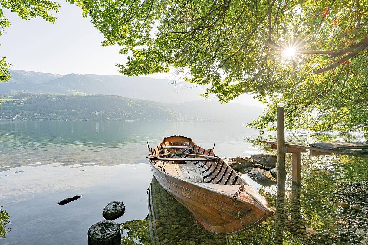 Ruderboot liegt vertäut im spiegelglatten Wasser am naturbelassenen am Ufer des Millstätter Sees