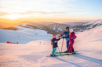 Familie steht mit Ski auf Piste am Falkert