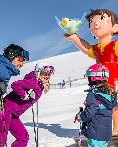 Familie steht mit Ski vor Heidifigur am Falkert