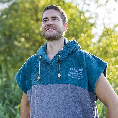 Junger Mann mit dem Badeponcho in blau grau mit dem Logo vorne an der Brust