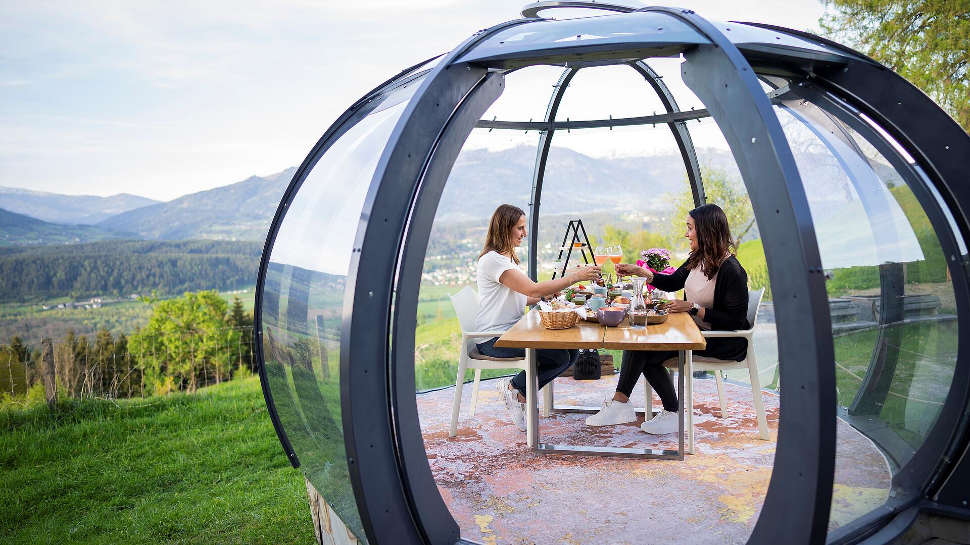 2 Personen sitzen in der Glaskuppel und genießen ihren Brunch an einem schönen Sommertag