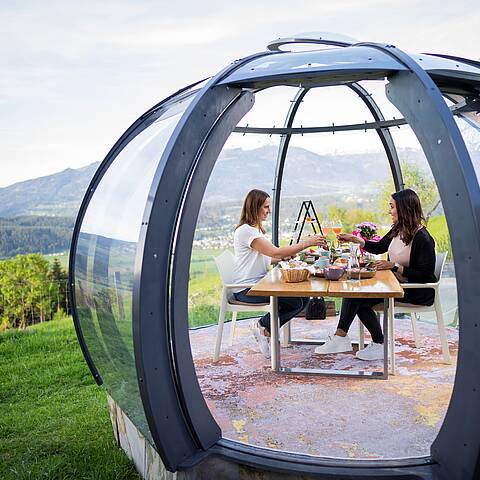 2 Personen sitzen in der Glaskuppel und genießen ihren Brunch an einem schönen Sommertag