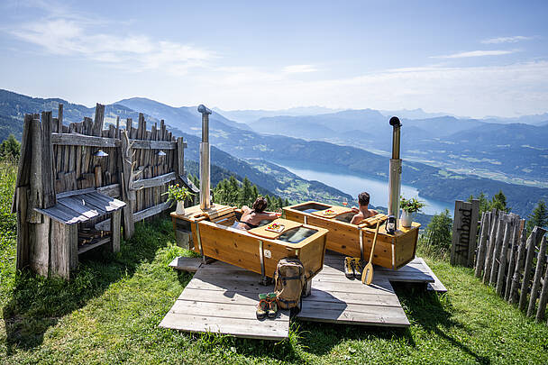 Ein Paar genießt ein AlmBad auf der AlexanderAlm mit Blick auf den Millstätter See.