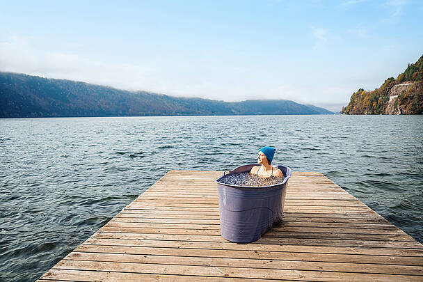 Frau liegt in Badewanne, die mit Eiswasser gefüllt ist, auf einem Holzsteg am Millstätter See