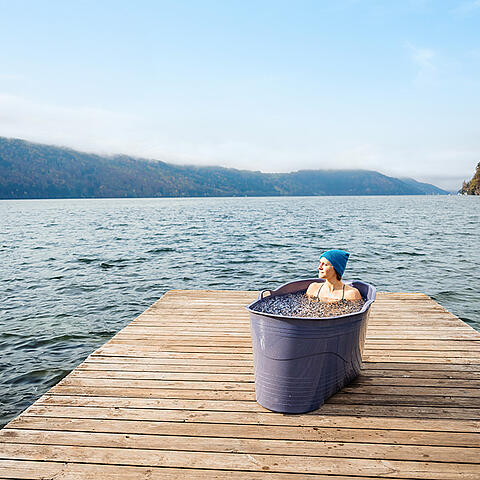 Frau liegt in Badewanne, die mit Eiswasser gefüllt ist, auf einem Holzsteg am Millstätter See