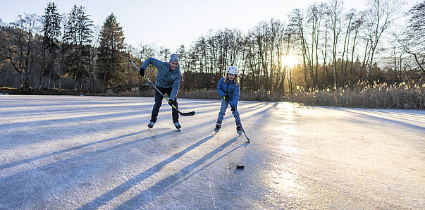 Erwachsener und Kind spielen Eishockey am Flatschacher See