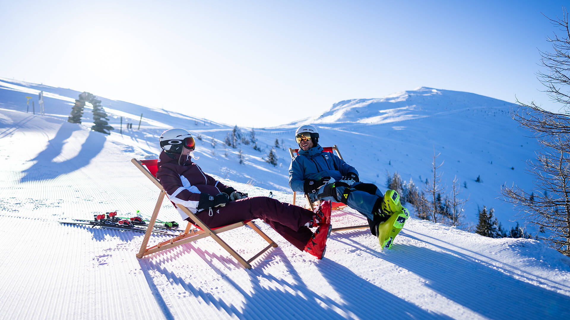 Liegestuhl-Pause Kaiserburg – Skigebiet Bad Kleinkirchheim Zwei Erwachsene im Liegestuhl auf der Kaiserburg mit Wöllaner Nock im Hintergrund im Skigebiet Bad Kleinkirchheim