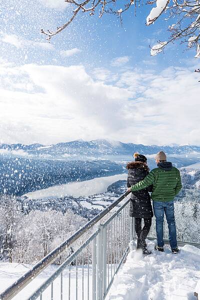 Pärchen stehth im Winter auf verschneitem Sternenbalkon mit Aussicht auf den Millstätter See