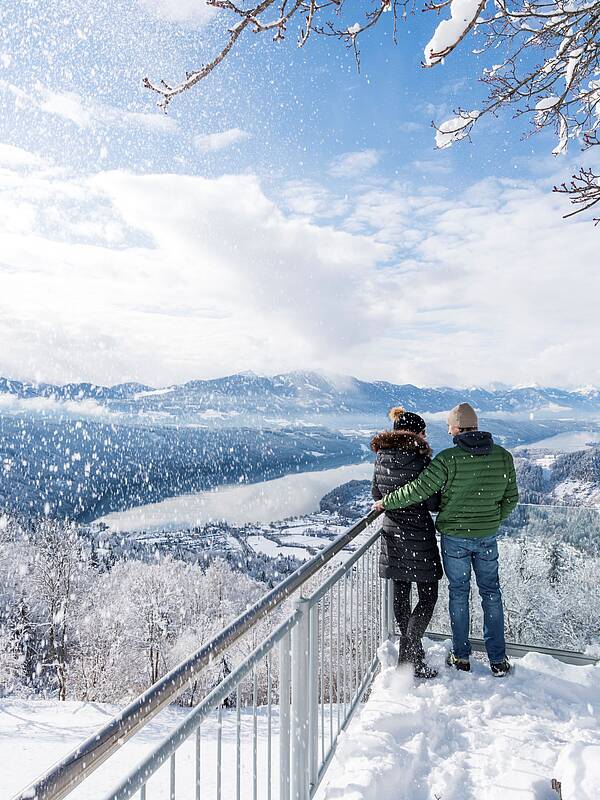 Pärchen stehth im Winter auf verschneitem Sternenbalkon mit Aussicht auf den Millstätter See
