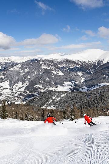Skifahrer fahren mit Bergpanorama im Hintergrund eine Piste im Skigebiet Bad Kleinkirchheim hinunter