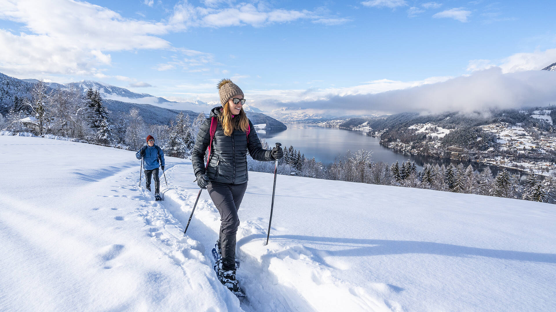 2 Personen gehen mit ihren Schneeschuhen am Mirnock mit dem Millstätter See im Hintergrund